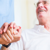 Elderly man looking up and smiling at a female Nurse who is holding his hand