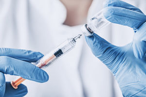 Female Nurse holding a needle that she is injecting into a tiny bottle